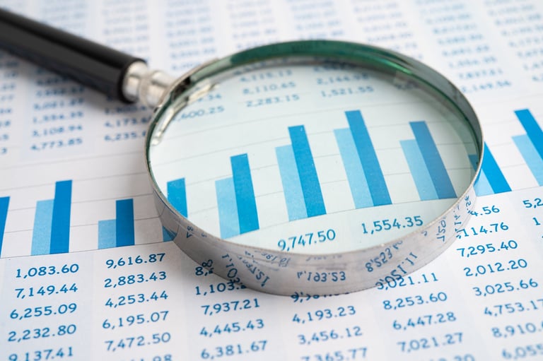 Magnifying glass on spreadsheet and graph paper showing cost analysis