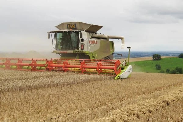 Combine harvester with red header attachment harvesting grain in a field with green countryside in background